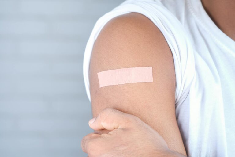 A close-up image of an adult with a bandage on the upper arm, likely after vaccination.